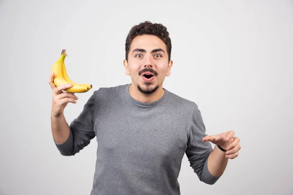 灰色の背景に熟したバナナを2つ持っている若い男 高品質の写真 — ストック写真