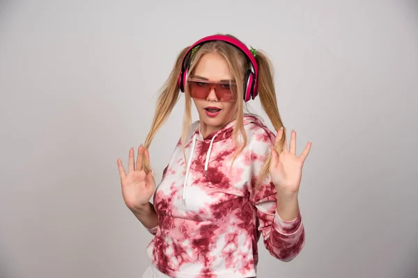 ピンクのヘッドフォンで髪で遊んでブロンドの若い女性 高品質の写真 — ストック写真