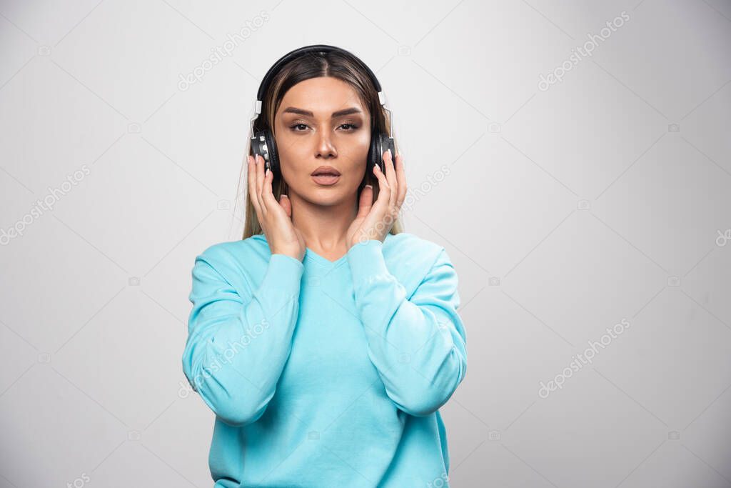 Blonde girl in blue sweatshirt wearing headphones and trying to understand the music. High quality photo