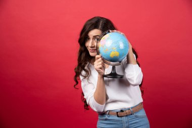 Kızıl arka planda, dünyanın arkasında saklanan esmer kadın. Yüksek kalite fotoğraf