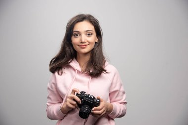 Gri bir duvarın üzerinde kamerayla duran güzel genç bir kadın. Yüksek kalite fotoğraf