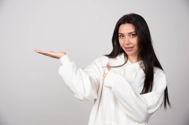 Beyaz kapüşonlu, el ve baş parmağını kaldırmış genç bir kadın modeli. Yüksek kalite fotoğraf