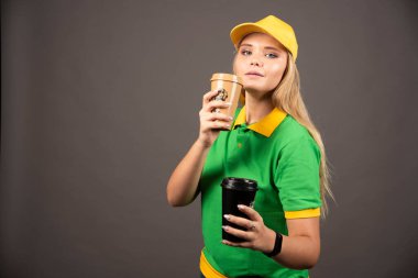 Elinde koyu fonda kahve bardakları tutan genç teslimatçı kadın. Yüksek kalite fotoğraf