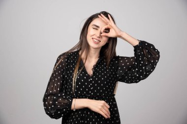 Güzel bir kadın iyi bir el hareketi yapıyor ve mutlu yüzüyle parmaklarının arasından bakıyor. Yüksek kalite fotoğraf