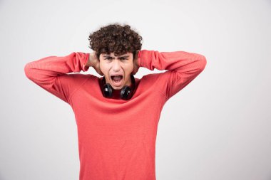 Kulaklıklı genç adam çığlık atarken kulaklarını kapatıyor. Yüksek kalite fotoğraf