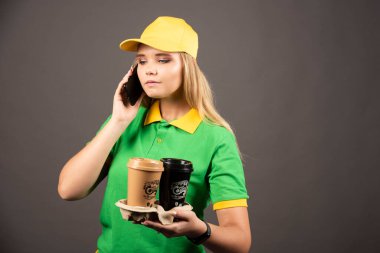 Elinde kahve fincanı olan teslimatçı kadın akıllı telefondan konuşuyor. Yüksek kalite fotoğraf