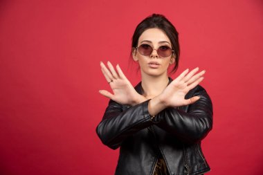 Siyah deri ceketli havalı kız bir şeyi durdurmak için ellerini ya da parmaklarını çaprazlıyor. Yüksek kalite fotoğraf