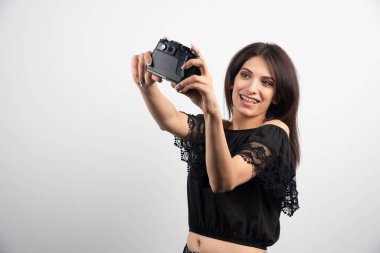 Esmer kadın beyaz arka planda fotoğraf makinesiyle selfie çekiyor. Yüksek kalite fotoğraf