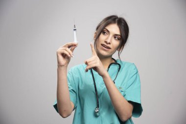 Kadın doktor gri arka plandaki şırıngayı işaret ediyor. Yüksek kalite fotoğraf