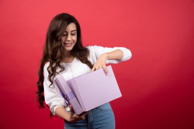 Kırmızı arka planda mor hediye kutusuna bakan güzel bir kadın. Yüksek kalite fotoğraf