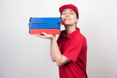 Beyaz arka planda üç kutu pizza tutan şapkalı genç teslimatçı kadın. 