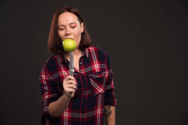 Sonbahar kış koleksiyonu giysileri içindeki kadın model bıçağın üzerinde yeşil bir elma ısırıyor. Yüksek kalite fotoğraf