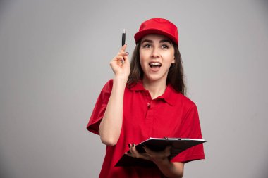 Kırmızı üniformalı teslimatçı kadın gri arka planda mutlu. Yüksek kalite fotoğraf