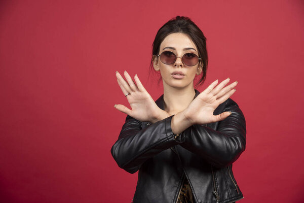 Cool girl in black leather jacket crossing hands or fingers to stop something. High quality photo