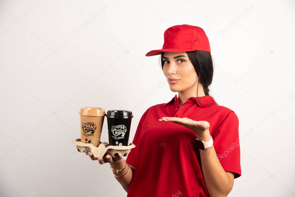 Female courier in uniform showing takeaways coffees. High quality photo