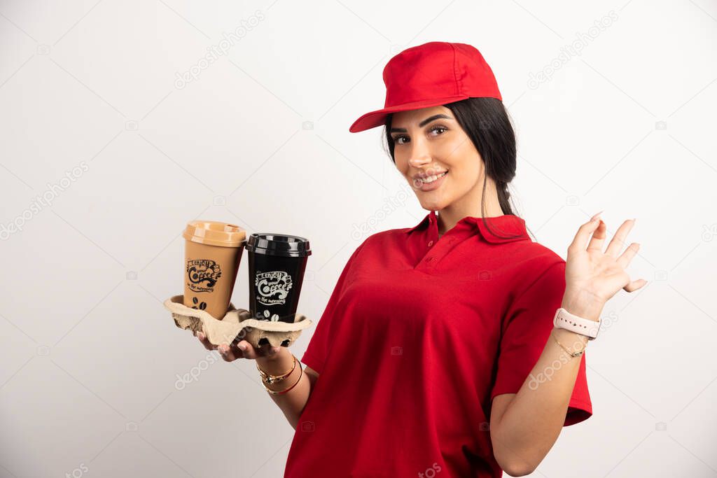Smiling courier in uniform holding takeaways coffees. High quality photo