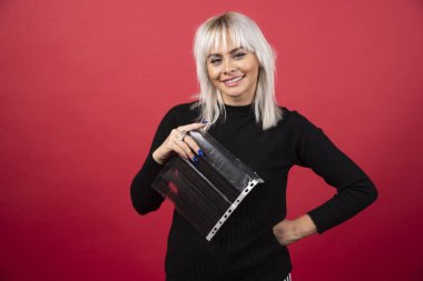 Kırmızı arka planda fotoğraf kasetiyle poz veren genç bir kadın. 