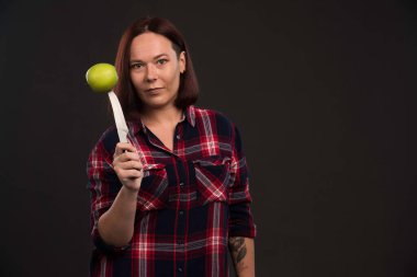 Sonbahar kış koleksiyonu giysileri içindeki kadın model yeşil bir elmanın üzerine bıçak koyuyor. Yüksek kalite fotoğraf