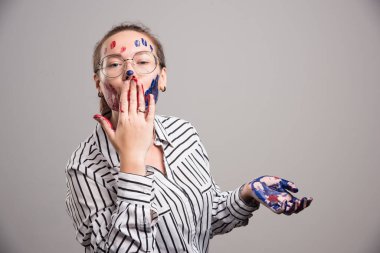 Yüzünde boya olan ve boyalı elleri gri arka planda olan bir kadın. Yüksek kalite fotoğraf