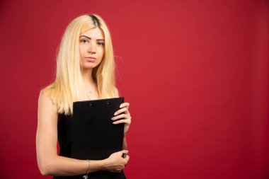 Genç çalışanın elinde dosya var ve kırmızı arka planda duruyor. Yüksek kalite fotoğraf