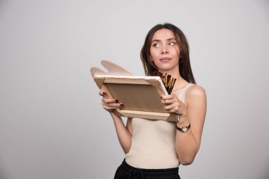 Gri arka planda boya aletleri tutan genç bir sanatçı. Yüksek kalite fotoğraf