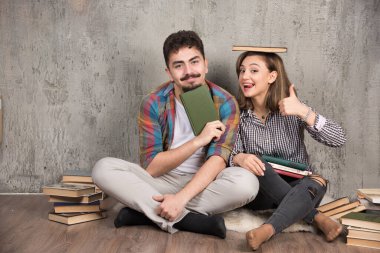 İki genç insan bir sürü kitapla poz veriyor ve başparmak kaldırıyor. Yüksek kalite fotoğraf