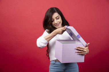 Kırmızı arka planda açık bir hediye tutan genç bir kadın. Yüksek kalite fotoğraf