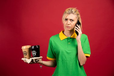 Telefonla konuşurken elinde kahve tutan teslimatçı kadın. Yüksek kalite fotoğraf