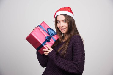 Noel Baba şapkalı gülümseyen kadın elinde yaylı bir Noel hediyesi tutuyor. Yüksek kalite fotoğraf