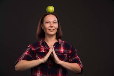 Sonbahar kış koleksiyonu giysileri içinde kafasında yeşil bir elma tutan ve dua eden bir kadın model. Yüksek kalite fotoğraf