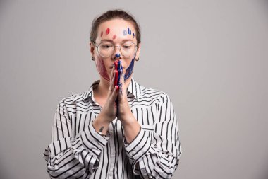 Yüzünde boya ve gri arka planda gözlük olan bir kadın. 