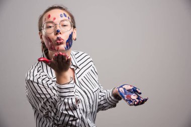 Yüzünde boya olan ve boyalı elleri gri arka planda olan bir kadın. Yüksek kalite fotoğraf