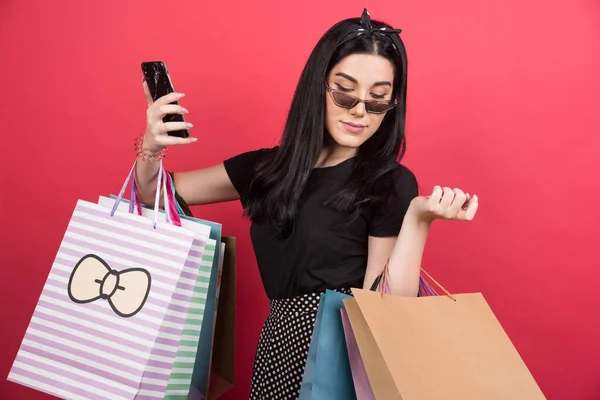 Jonge Vrouw Met Bril Houden Haar Tassen Telefoon Rode Achtergrond — Stockfoto