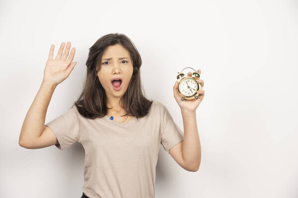Шокированная женщина держит будильник на белом фоне. Высокое качество фото