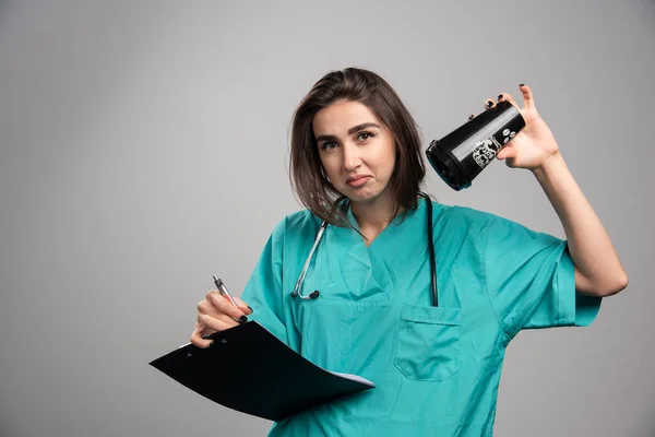 灰色の背景にカップとクリップボードを保持する若い医師 高品質の写真 — ストック写真