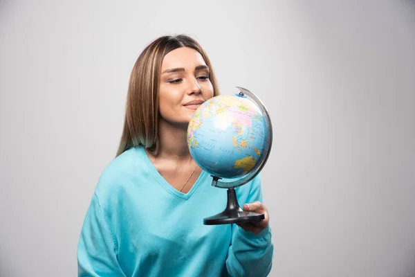 Blonde girl in blue sweatshirt holding a globe, guessing location and having fun. High quality photo