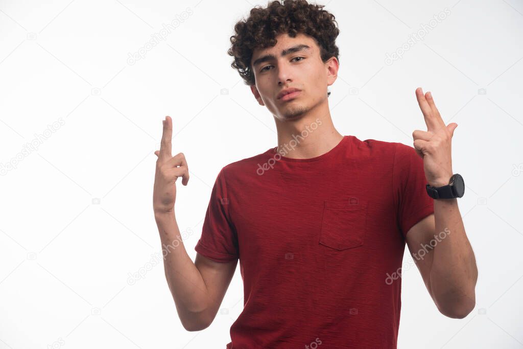Young boy with curly hairstyle makes gun sign. High quality photo