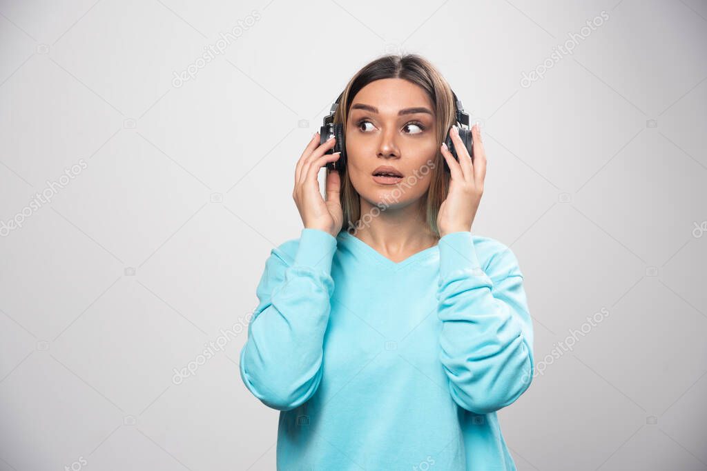 Blonde girl in blue sweatshirt wearing headphones and trying to understand the music. High quality photo