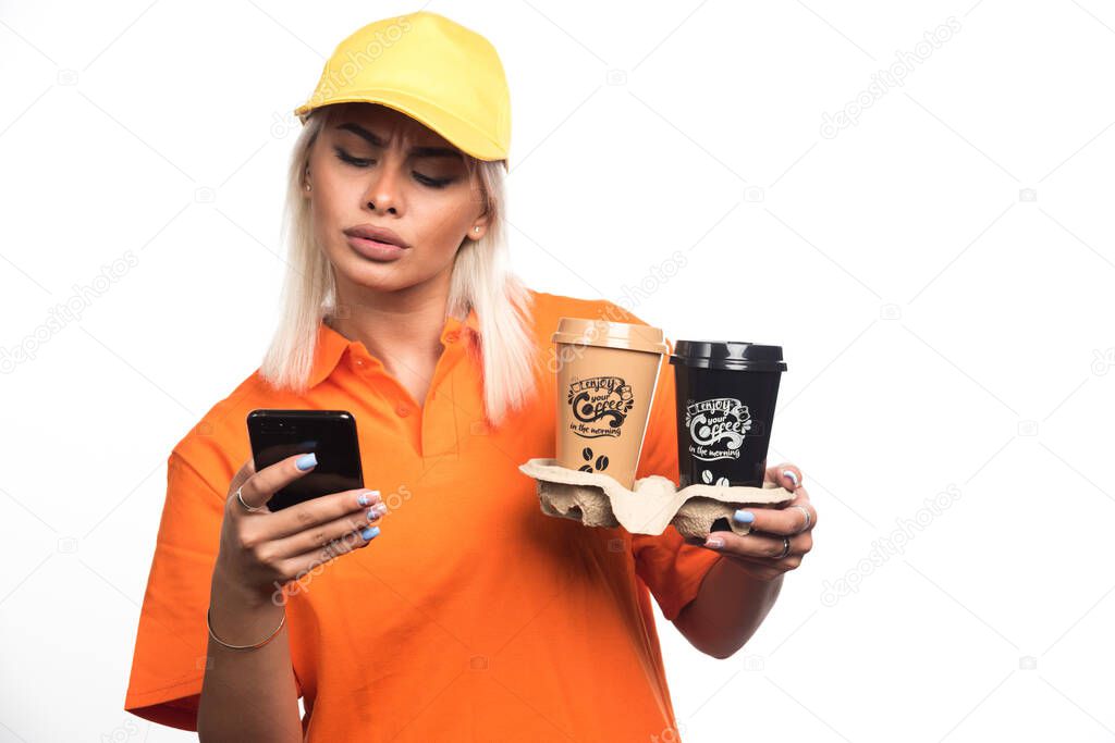 Female courier holding two cups of coffees on white background while using telephone. High quality photo