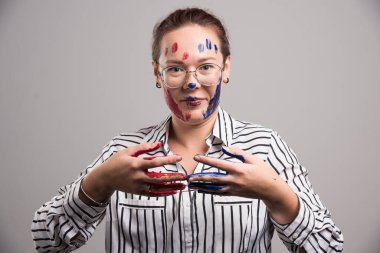 Yüzünde boya ve gri arka planda gözlük olan bir kadın. 