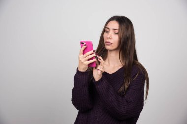 Pembe akıllı telefona bakan kalın kazaklı genç bir kadın. Yüksek kalite fotoğraf