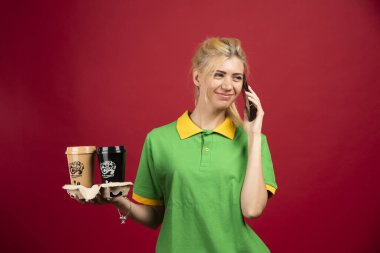 Kurye telefonda konuşurken iki fincan kahve tutuyor. Yüksek kalite fotoğraf