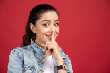 Kot ceketli genç bir kadın kırmızı arka planda tabela yapıyor. Yüksek kalite fotoğraf