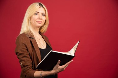 Kırmızı arka planda duran defterli genç bir iş kadını. Yüksek kalite fotoğraf