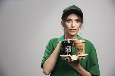 Kahve fincanlarıyla poz veren yeşil üniformalı teslimatçı kadın. Yüksek kalite fotoğraf