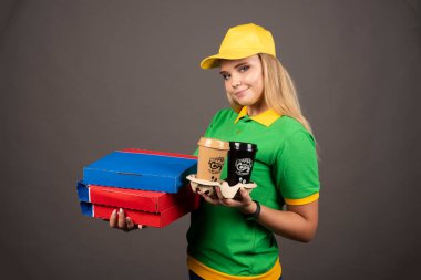 Elinde kahve ve pizza kartonlarıyla gülümseyen teslimatçı kadın. Yüksek kalite fotoğraf