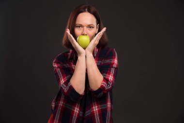 Sonbahar kış koleksiyonu giysileri içinde, ağzında yeşil bir elma tutan bir kadın model. Yüksek kalite fotoğraf