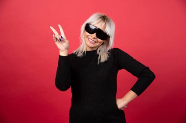 Kırmızı arka planda siyah gözlüklü, ayakta duran ve poz veren kadın portresi. Yüksek kaliteli fotoğraf.
