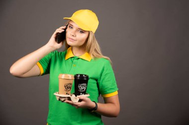 Elinde bir fincan kahveyle akıllı telefondan konuşan genç teslimatçı kadın. Yüksek kalite fotoğraf