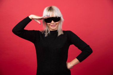 Kırmızı arka planda siyah gözlüklü, ayakta duran ve poz veren kadın portresi. Yüksek kaliteli fotoğraf.